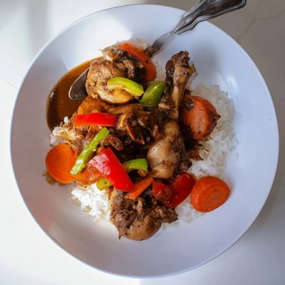 Tender Jamaican brown stew chicken served over steamed white rice with thick, deeply colored sauce