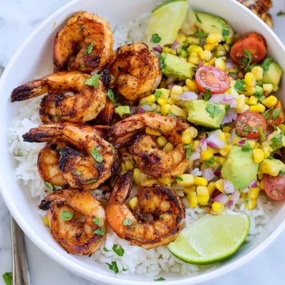 Smoky grilled shrimp bowl topped with bright avocado corn salsa and lime wedges