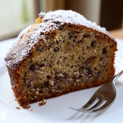 Moist banana cake with scattered walnuts served warm on a rustic cutting board
